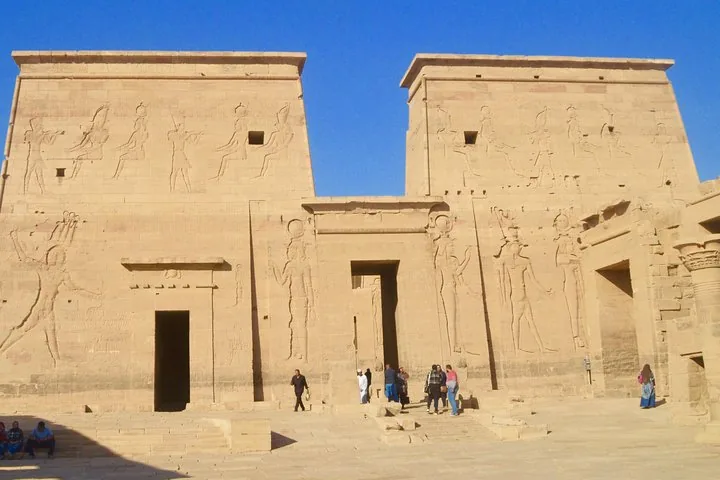 Touristen stehen vor der beeindruckenden Fassade des Philae-Tempels, die mit großen Reliefs verziert ist.